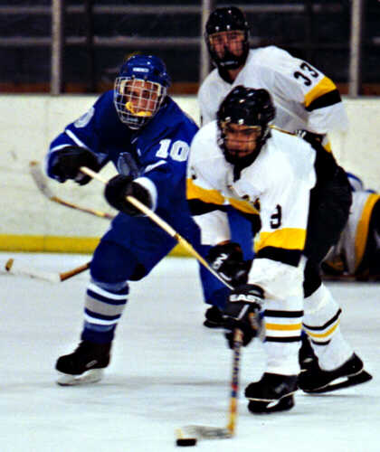 Lee Allen holds the puck just out of reach of a Trinity Trojan.